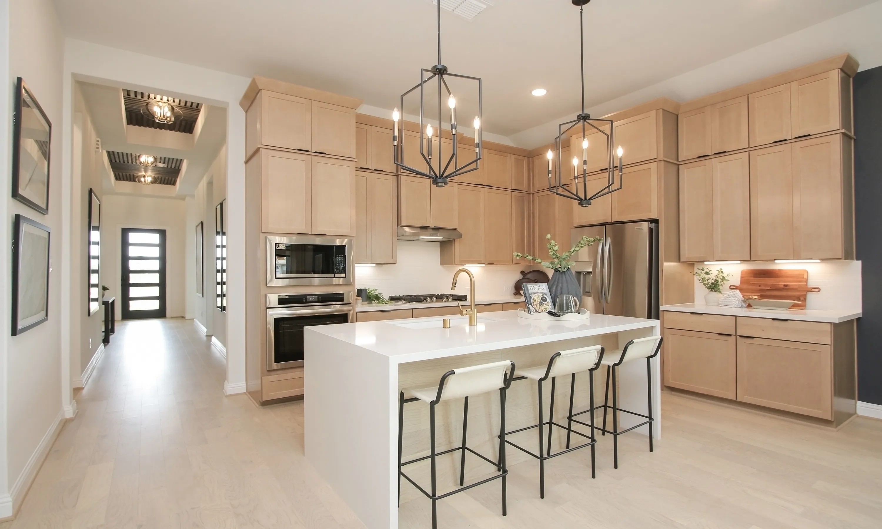 Modern Kitchen in Coastal Point Community with Light Wood Features Modern kitchen, light wood cabinets, island with gold faucet, Coastal Point community, sleek design.