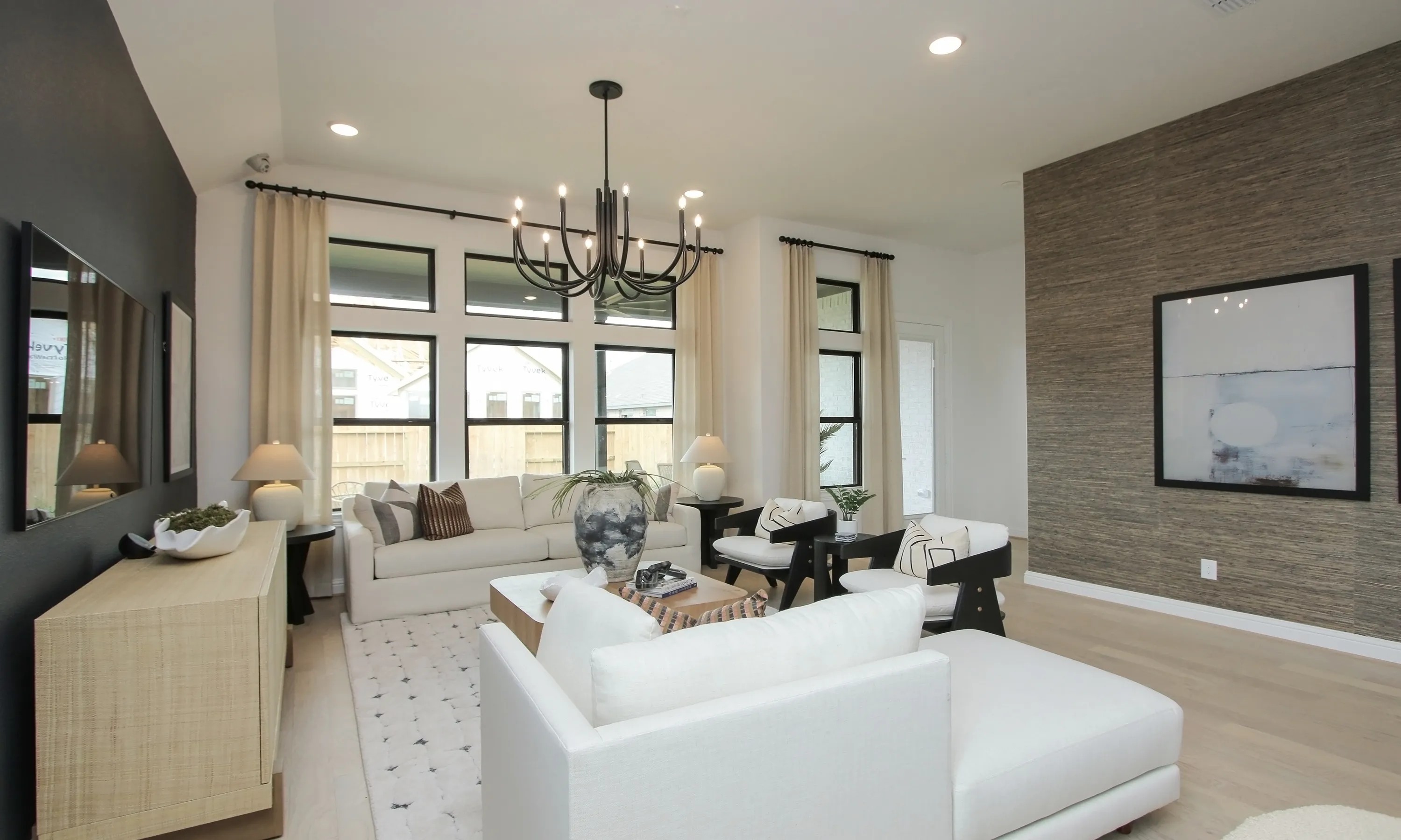 Coastal Point Living Room with Modern Chandelier and Large Windows Elegant living room in Coastal Point community with modern chandelier, large windows, textured accent wall, neutral decor.