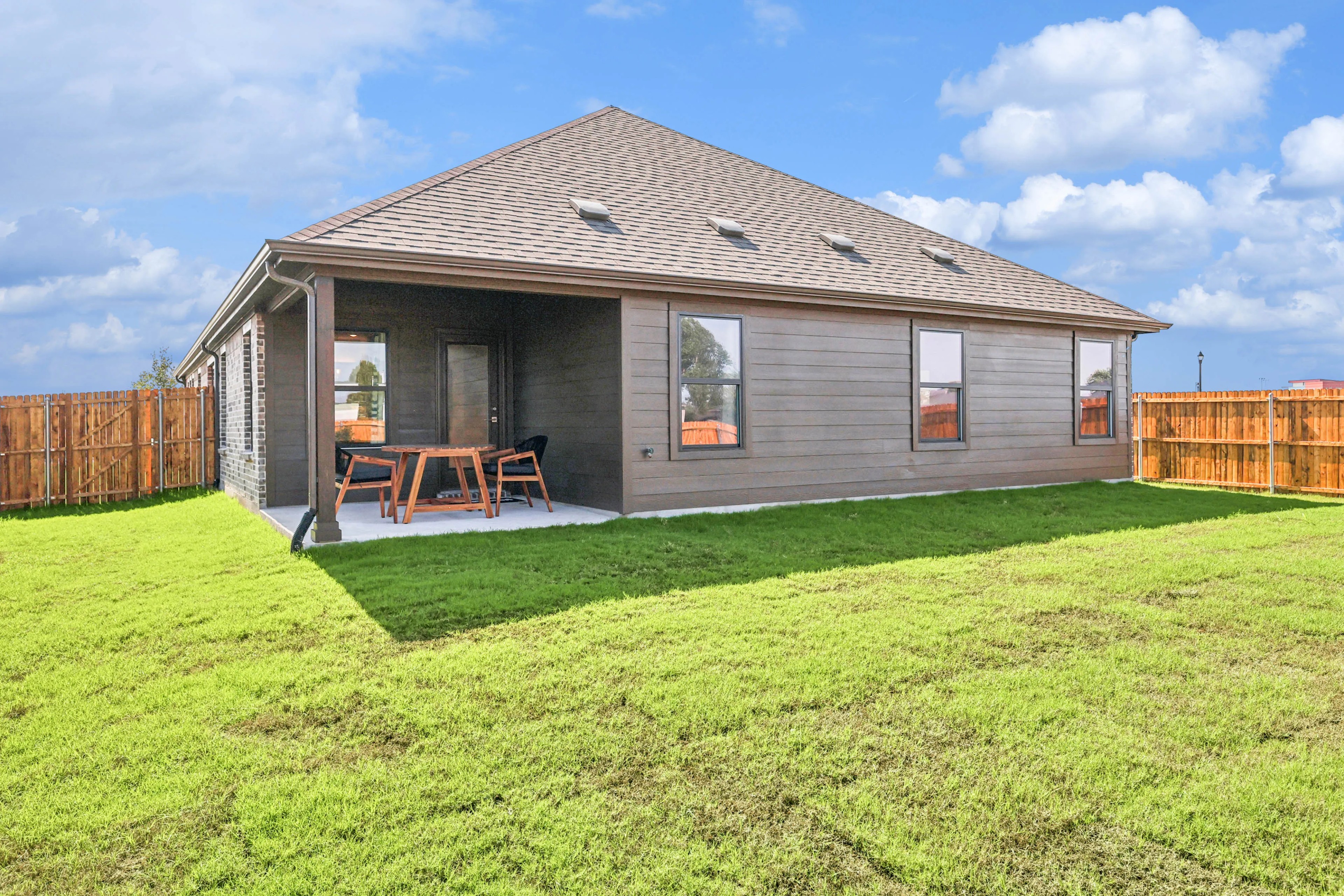 Pebblebrook Home Patio with Wood Siding and Lawn Backyard with covered patio, wood siding, and sloped roof in Pebblebrook community. Fenced yard, open sky.