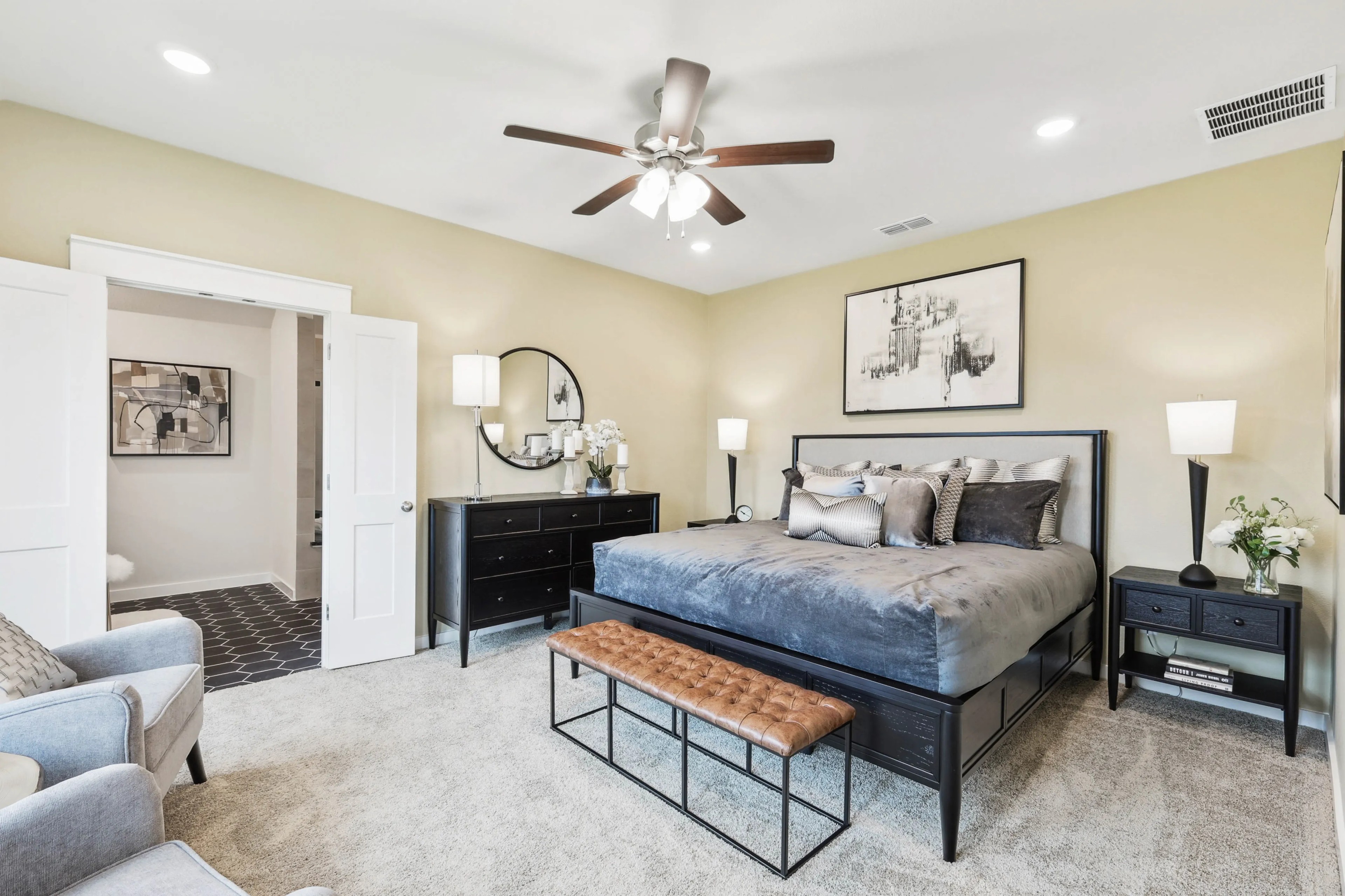 Elegant Bedroom with Modern Dark Furniture in Simpson Crossing Luxury bedroom with beige walls, dark furniture, and plush bedding in Simpson Crossing. Wall art and ceiling fan present.